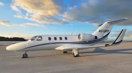 A white Cessna CitationJet with black and blue stripes, tail number N513RV, parked on a tarmac at sunset.