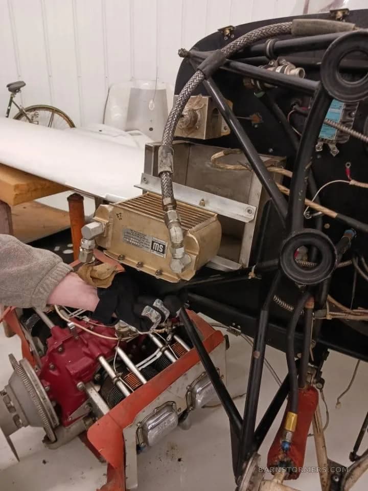 A close-up view of an aircraft engine being worked on, showing a person's hand near the red engine block.