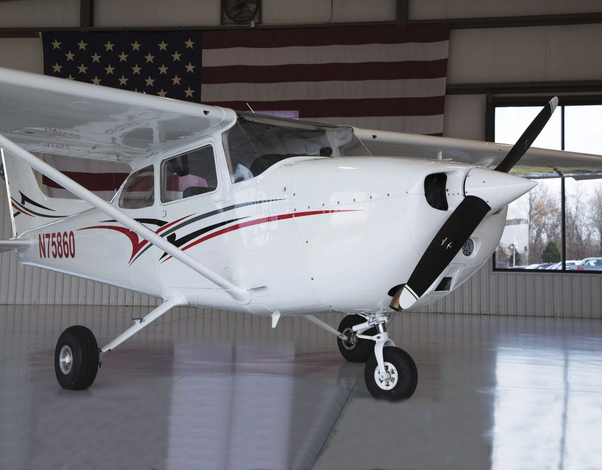 Cessna 172 Skyhawk parked in a hangar with an American flag in the background.
