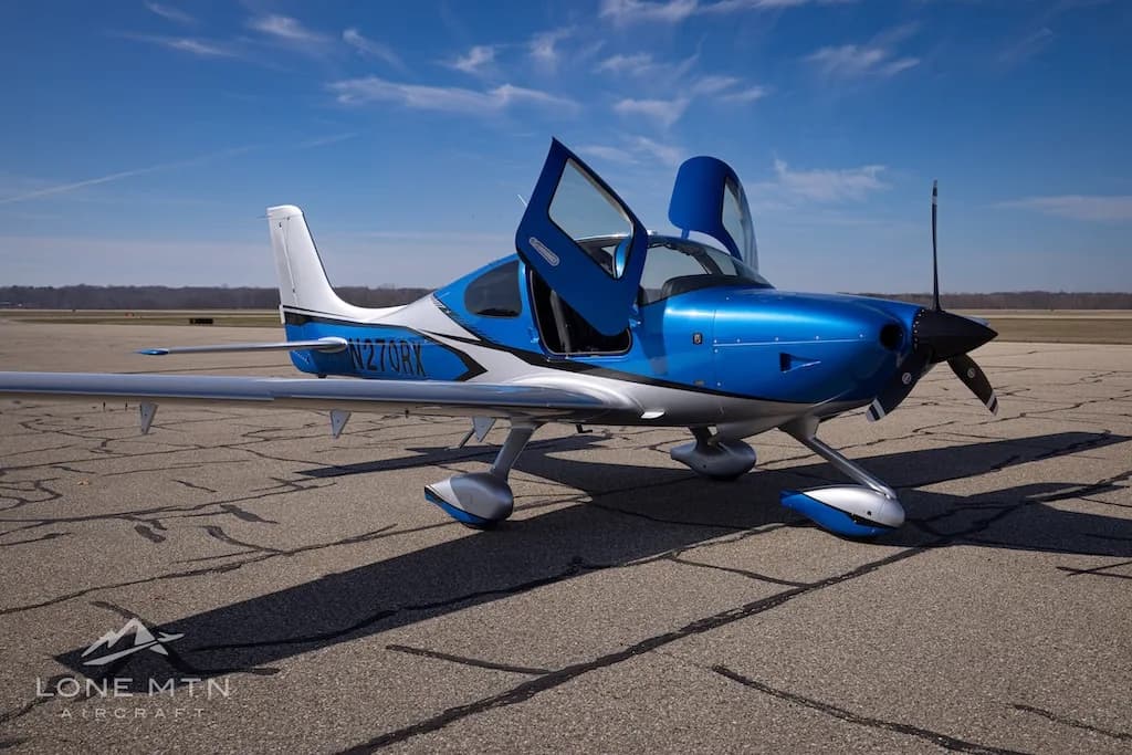 A front-side view of the blue and silver Cirrus SR20 aircraft, registration N270RX, with its doors open on an airport tarmac.