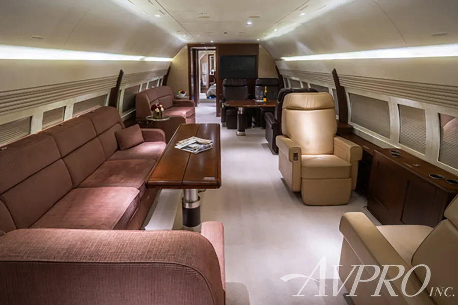 A spacious aircraft cabin with brown sofas, beige armchairs, and wooden tables.
