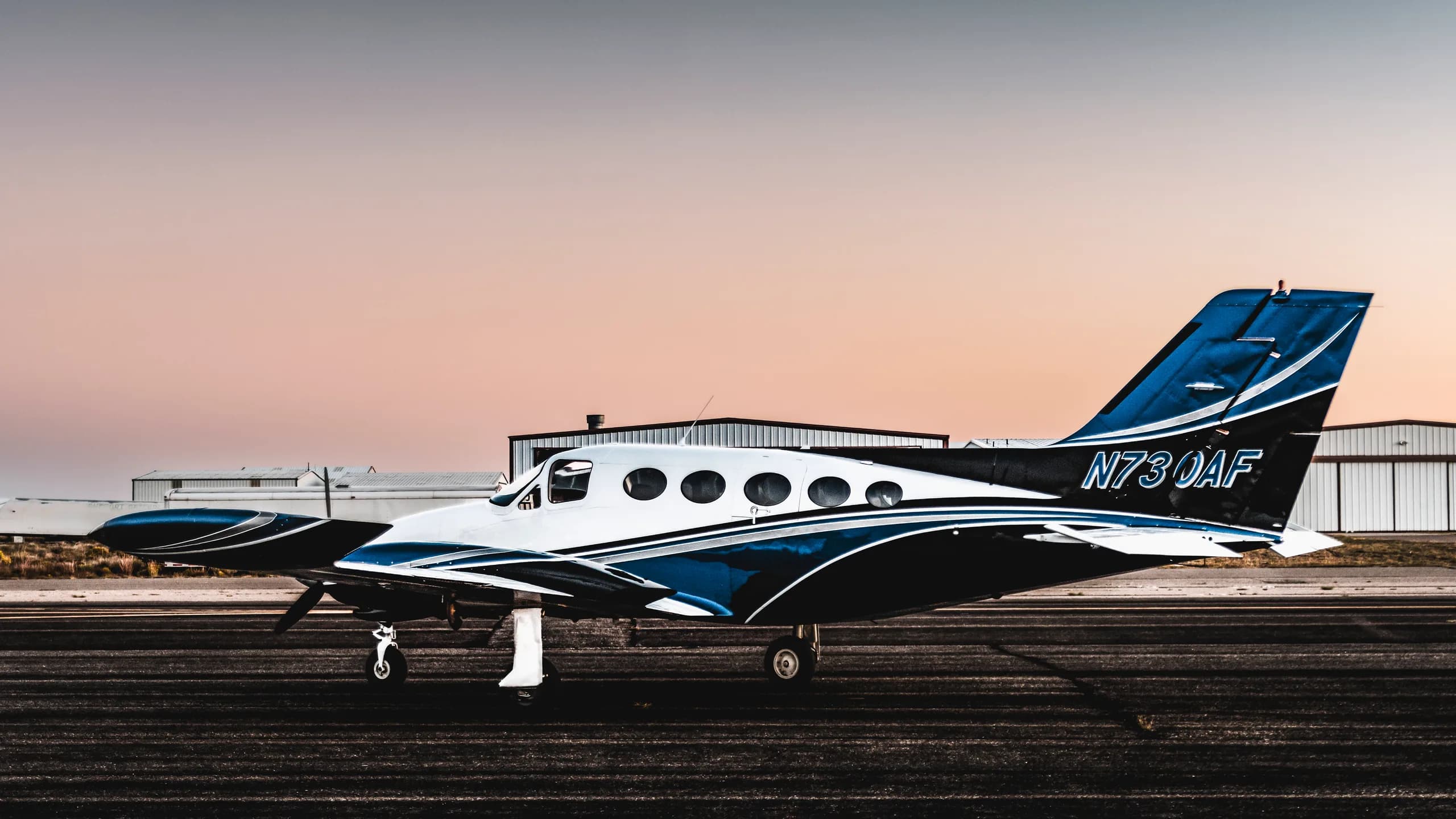 A white and blue twin-engine aircraft with registration N730AF, parked on a runway at sunset.