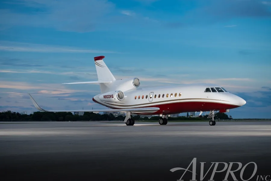 A Dassault Falcon 900LX, registration N900VG, parked on the tarmac under a blue sky with a white and red paint scheme.