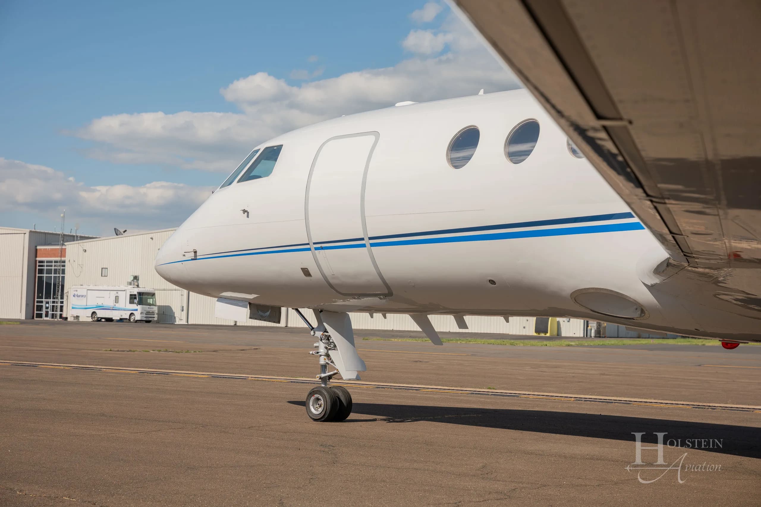 A close-up view of the nose and front landing gear of the white Dassault Falcon 900EX, N346EX, on an airfield.