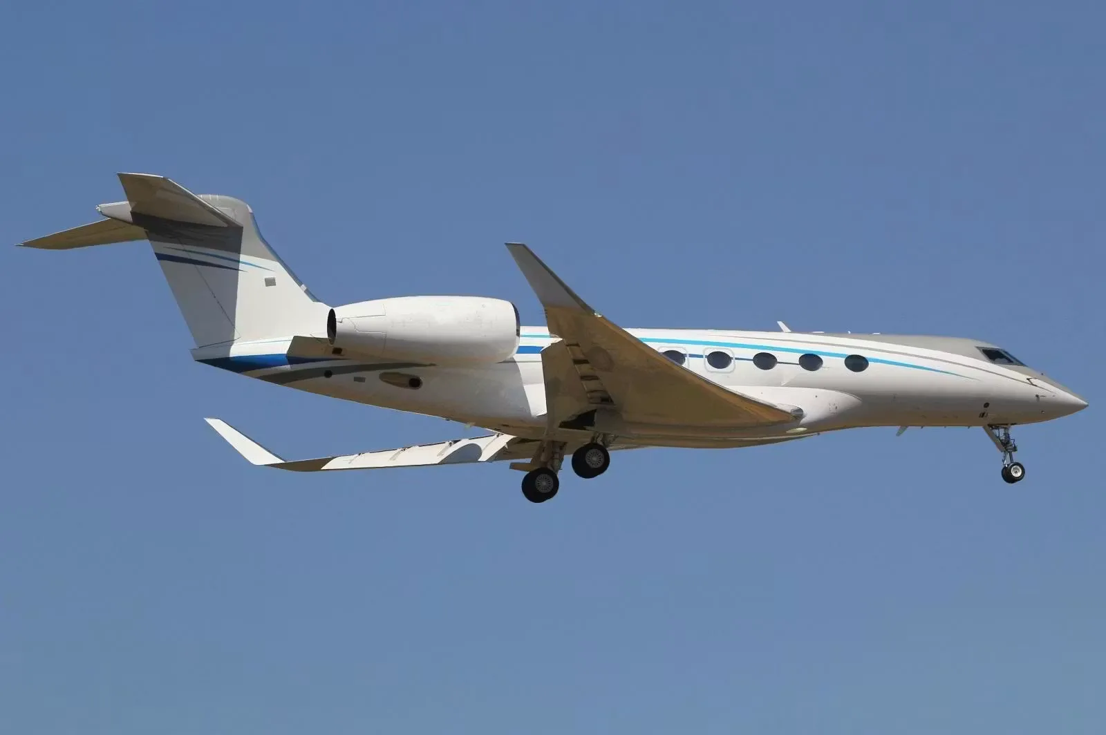 A white and silver Gulfstream business jet is in flight against a clear blue sky.