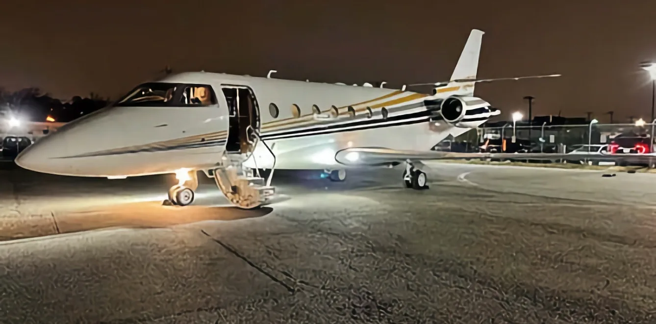 A white and gold jet with its door open sits on the tarmac at night.