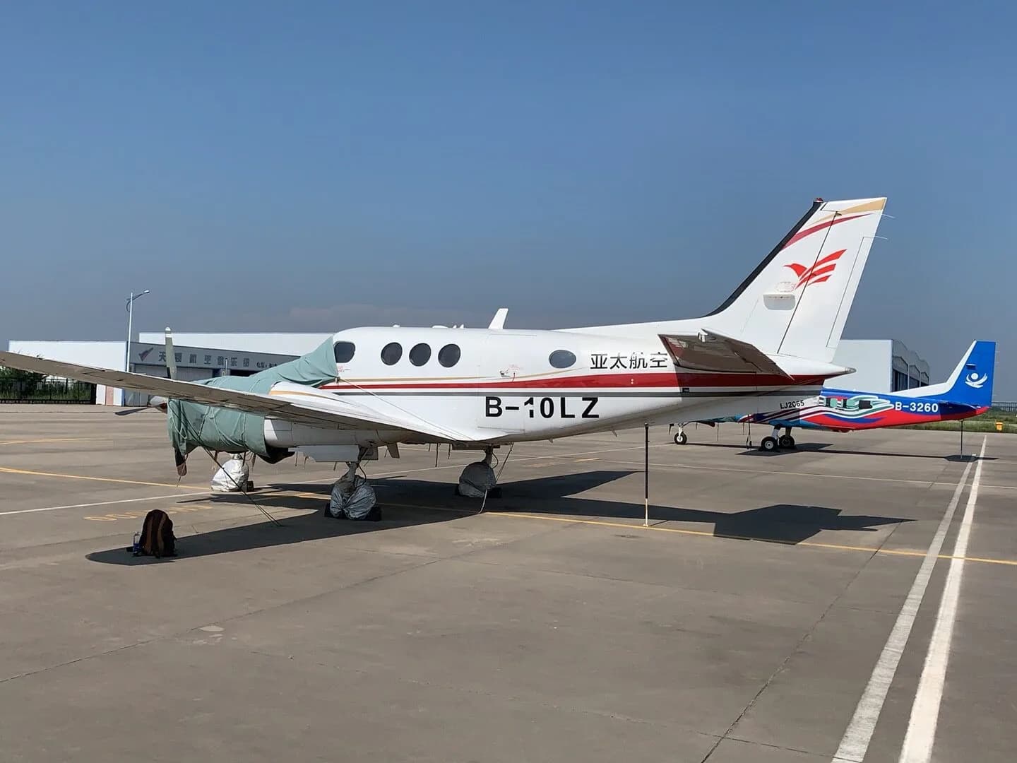 A King Air B-10LZ aircraft is parked on the tarmac with propeller covers, with another aircraft in the background.