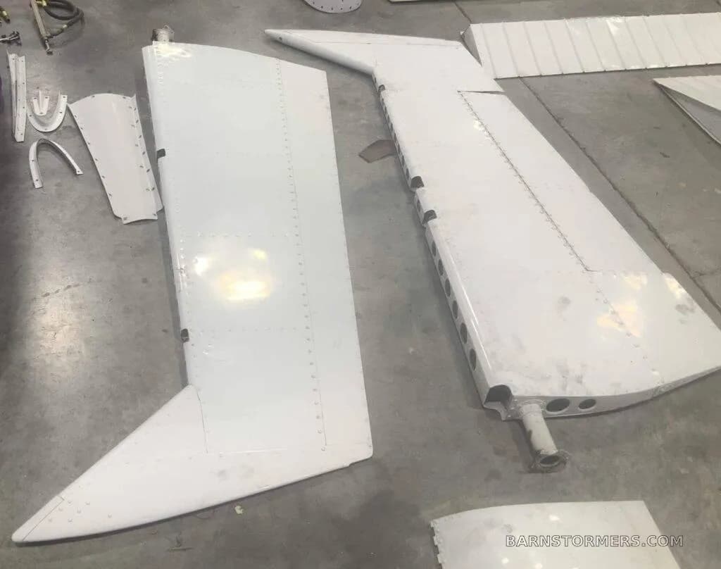 Disassembled white aircraft tail components, including a horizontal stabilizer and elevator, laid out on a concrete floor.