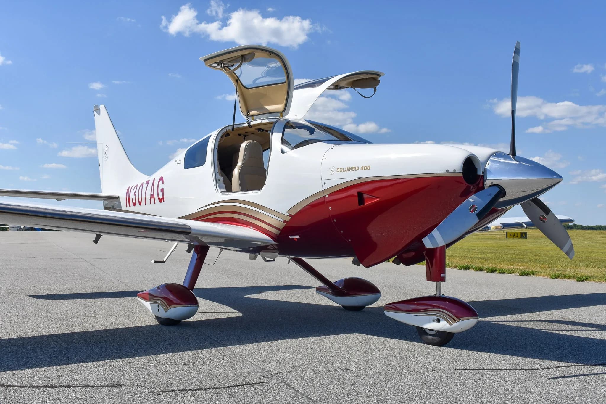 Three-quarter front view of a white and maroon Columbia 400 aircraft with registration N307AG and open doors on an airfield.