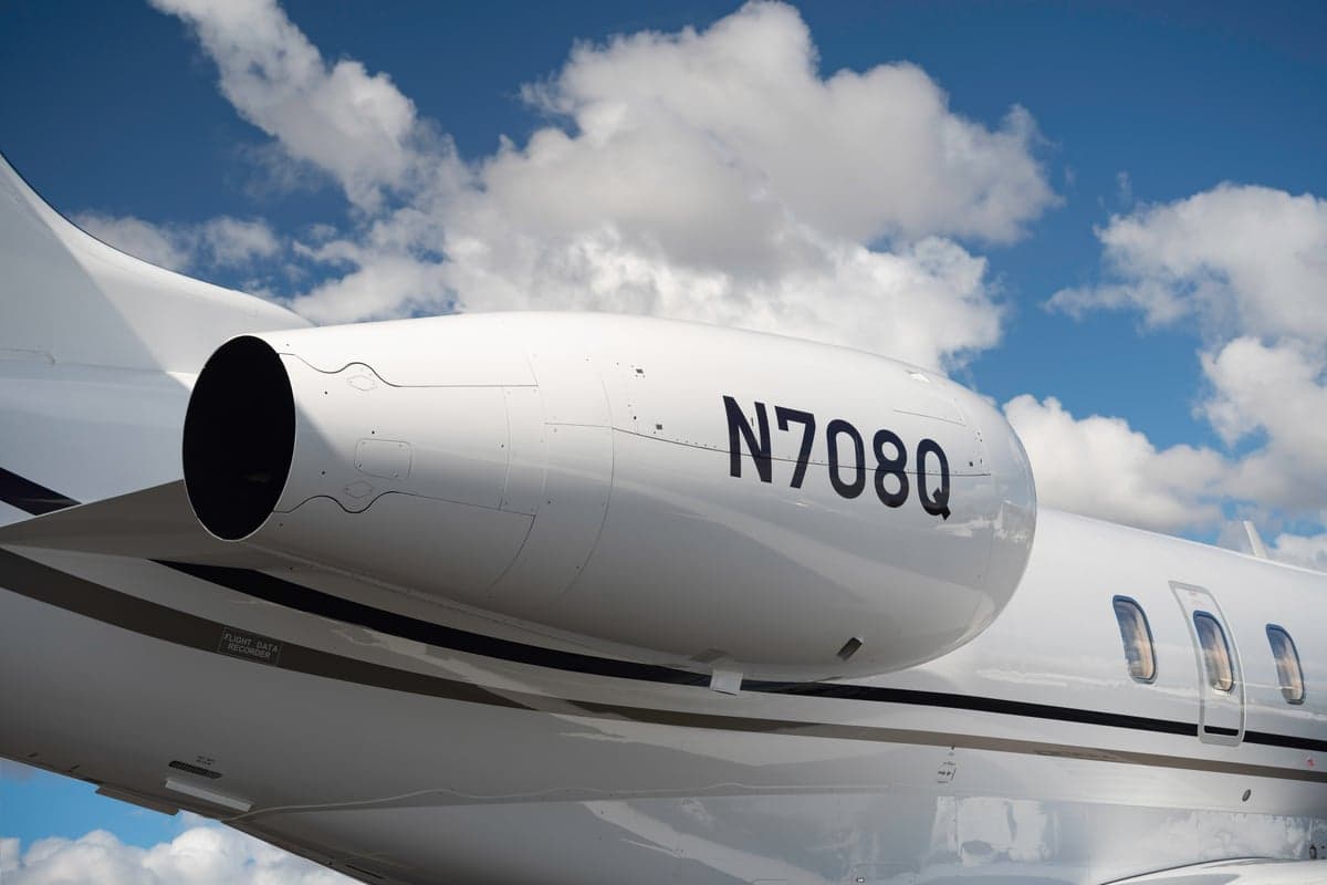 A side view of the rear-mounted engine and fuselage of a white business jet with the registration N708Q.