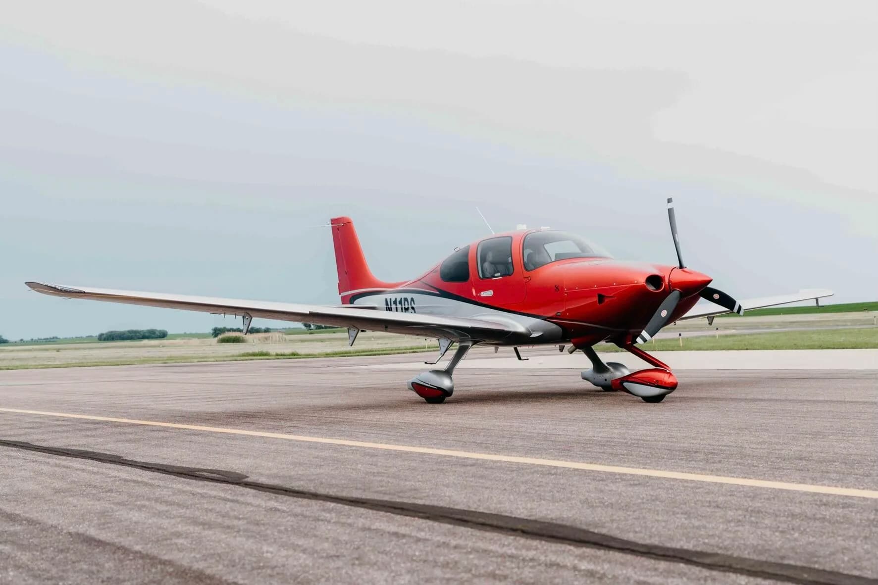 A red and silver Cirrus SR20 Premium aircraft (N11PS) parked on an airfield tarmac.