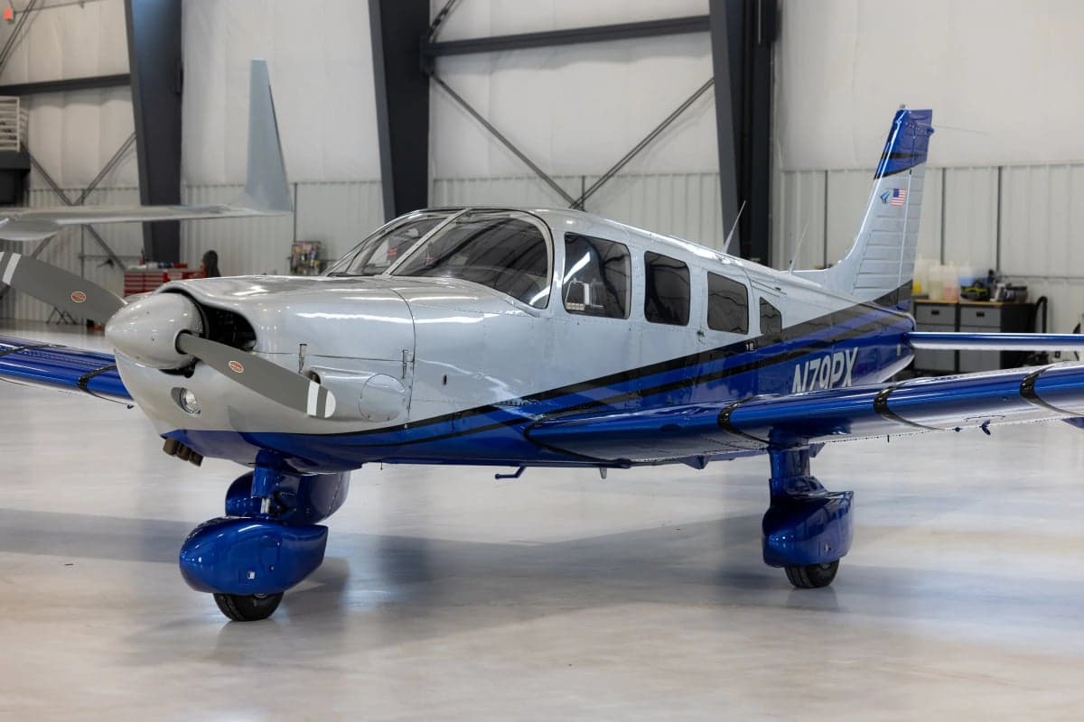 A Piper PA-28 Cherokee with a silver and blue paint scheme parked in a hangar.