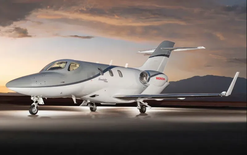 A HondaJet aircraft in a grey and white paint scheme, parked on a tarmac at sunset.