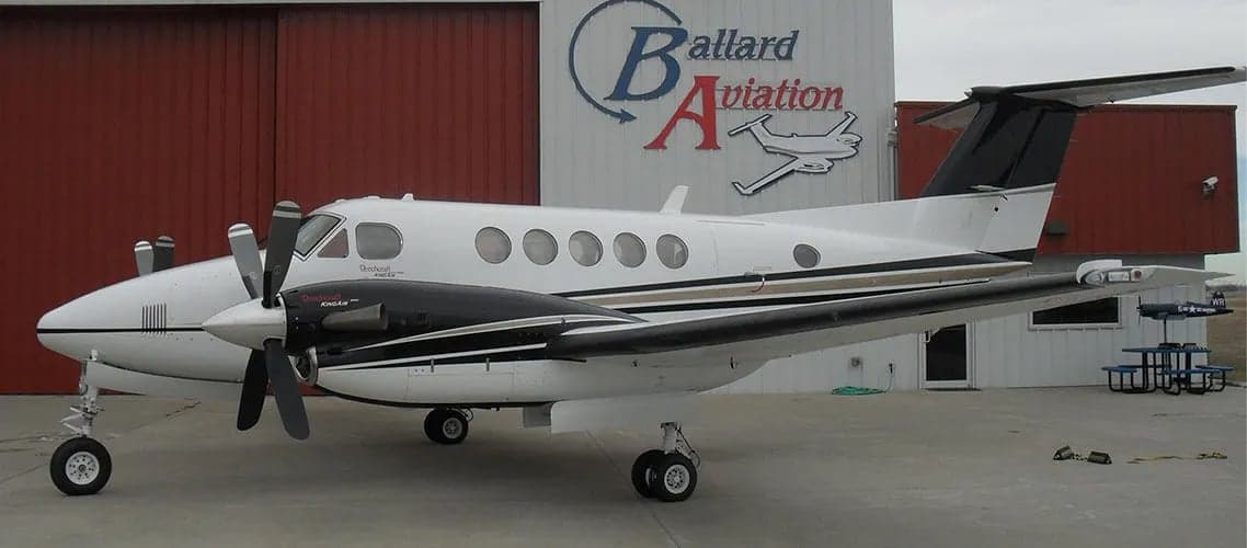 King Air aircraft parked in front of a hangar with the Ballard Aviation logo.