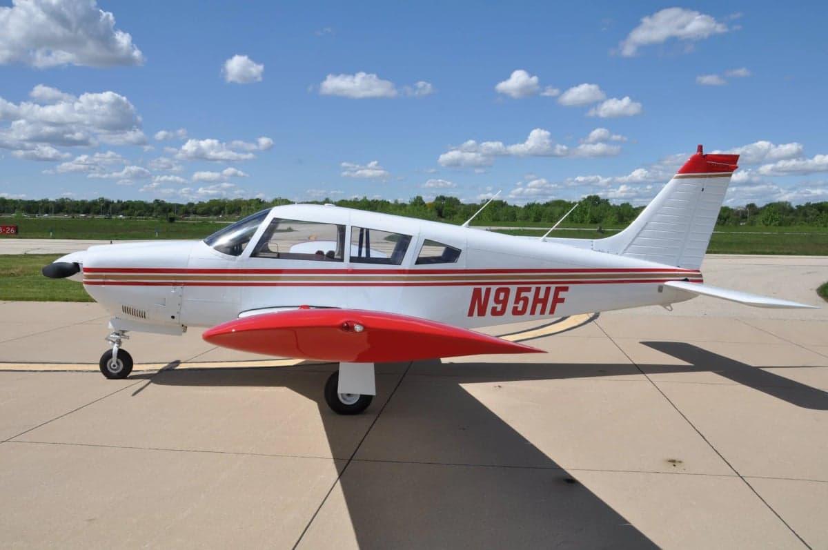 A side view of a white single-engine aircraft with red and gold stripes and registration N95HF on the fuselage.