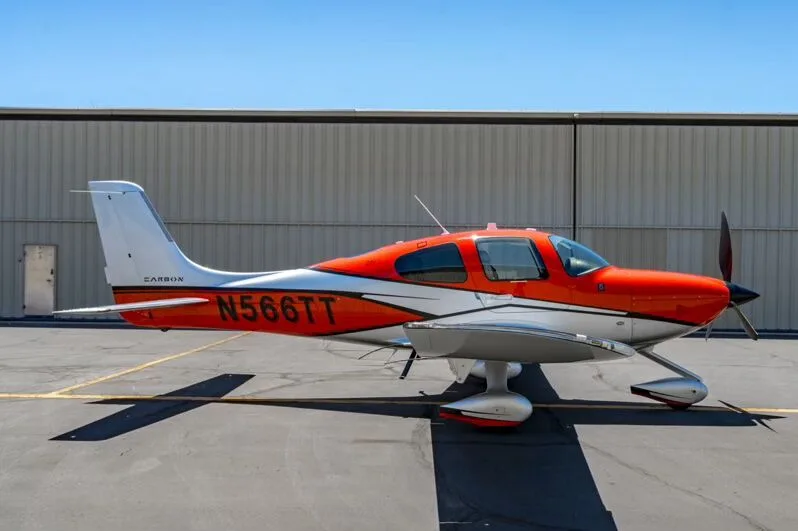 Side view of a red and silver Cirrus SR22T aircraft (N566TT) parked on an airfield.