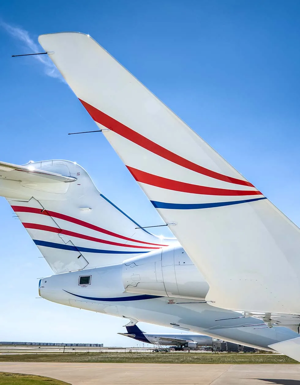 A close-up view of the white tails of multiple aircraft, featuring red and blue stripe liveries.