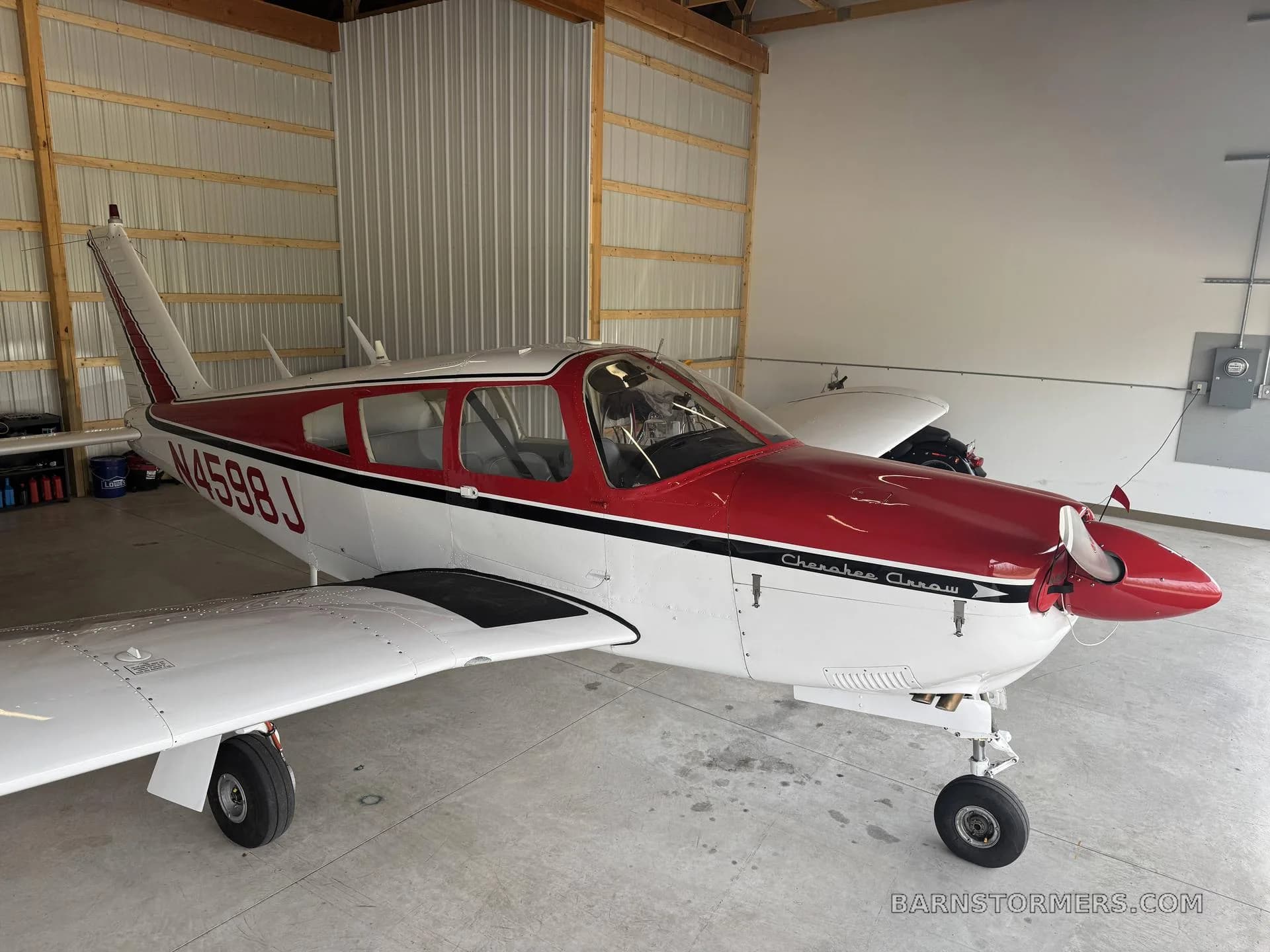 A red and white Piper Cherokee Arrow aircraft, registration N4598J, viewed from the front-right inside a hangar.