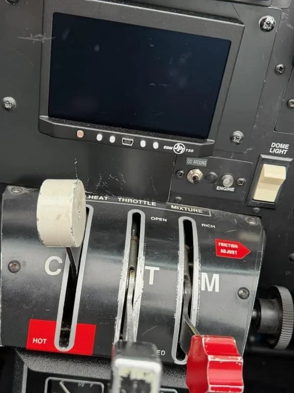 A close-up view of the throttle, propeller, and mixture controls, along with an engine monitor display in an aircraft cockpit.