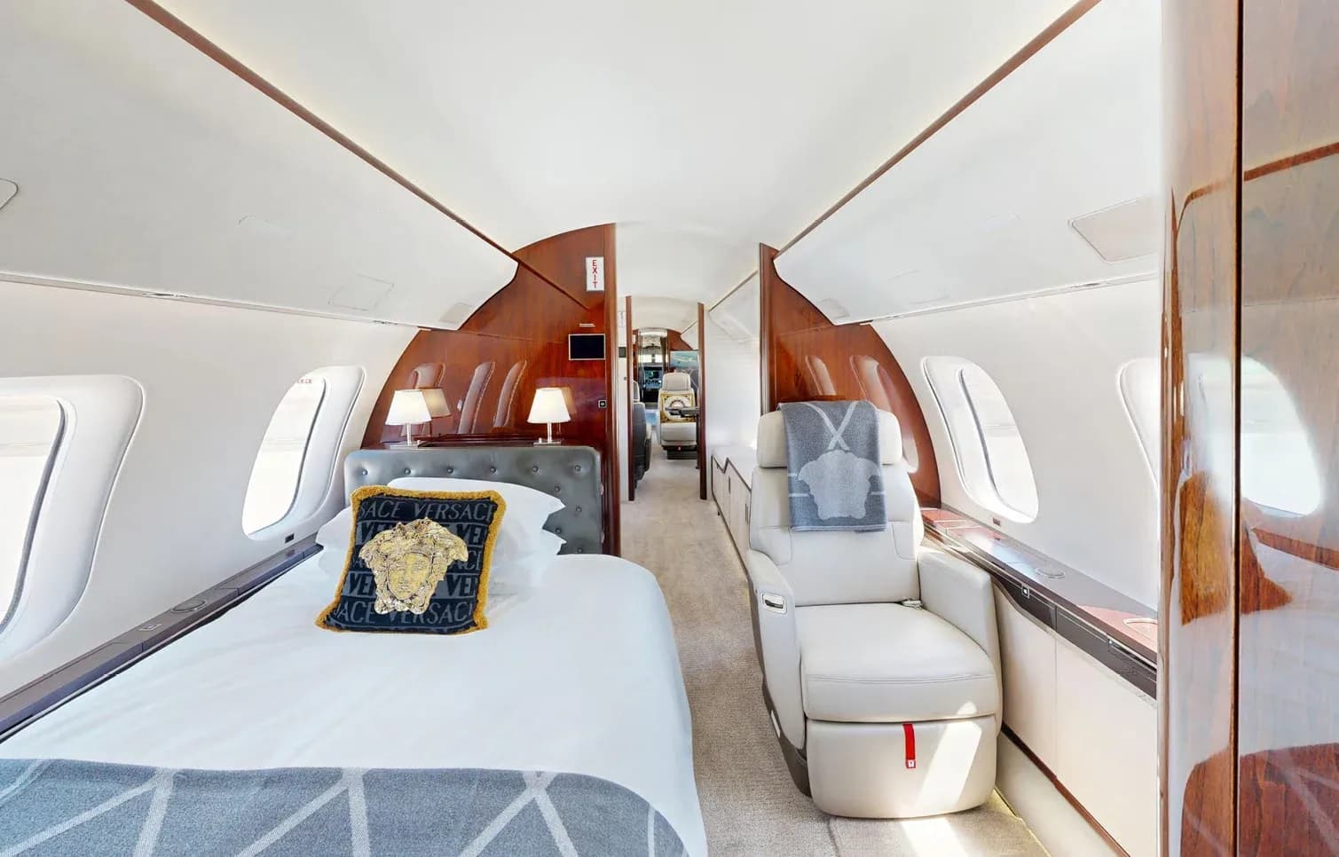 The private jet's cabin featuring a comfortable bed with a Versace pillow and a single plush seat.