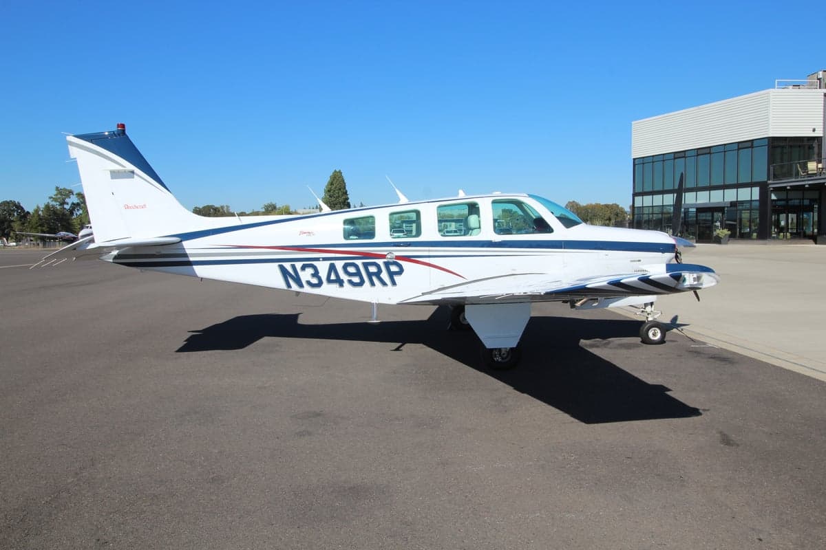 A Beechcraft Bonanza is parked on the tarmac on a sunny day.