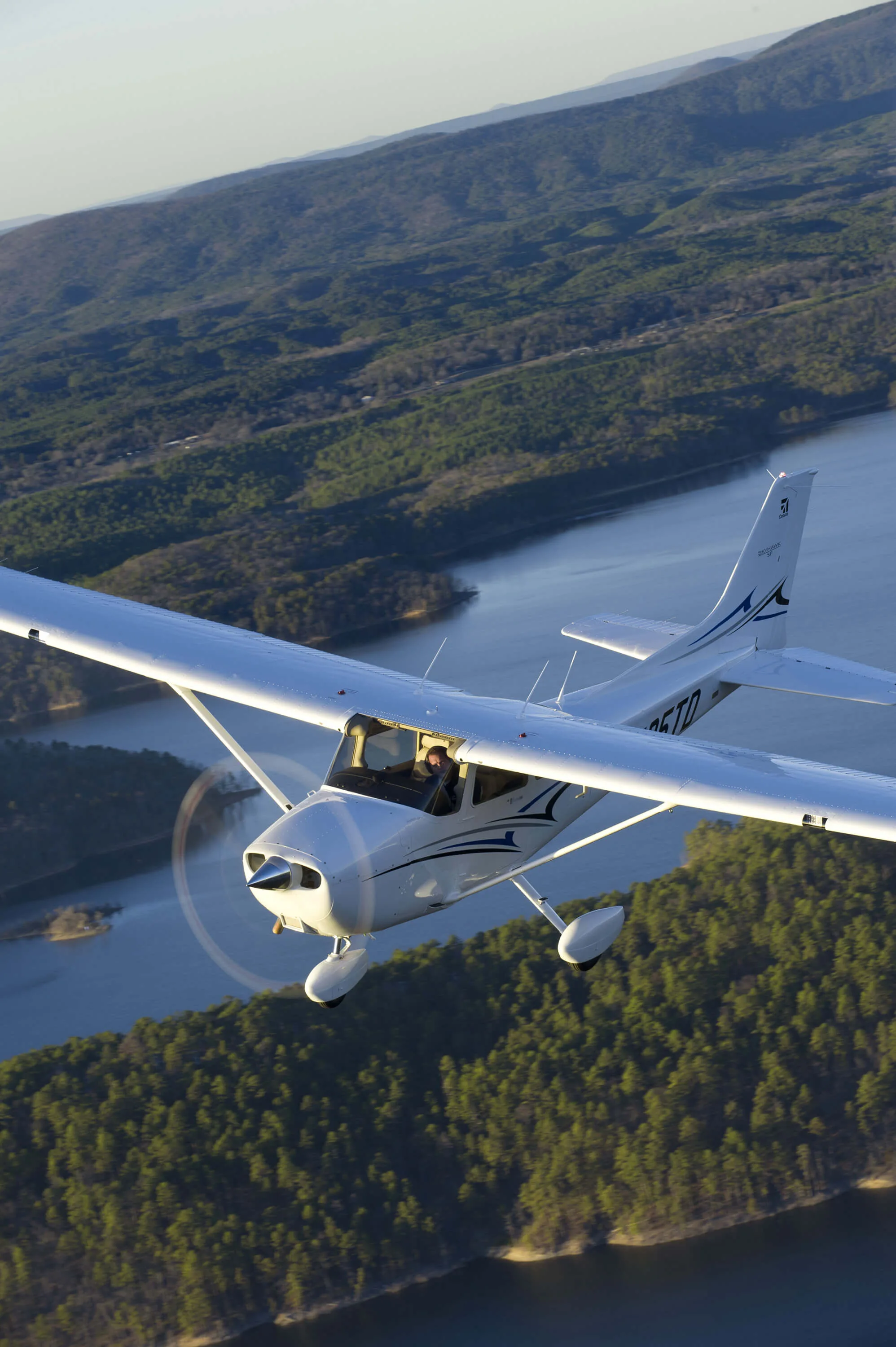 A Cessna 172 Skyhawk in flight over a mountainous, wooded area.