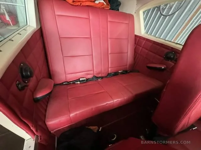 The rear red leather bench seat of a small aircraft cabin with quilted side panels.