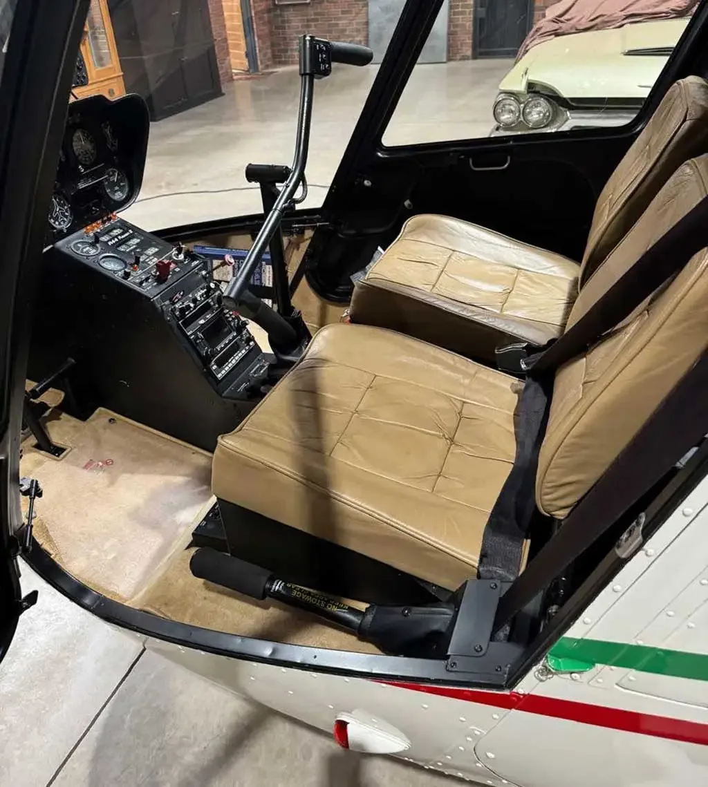 The tan leather interior and partial cockpit controls of a helicopter are visible from the open door.