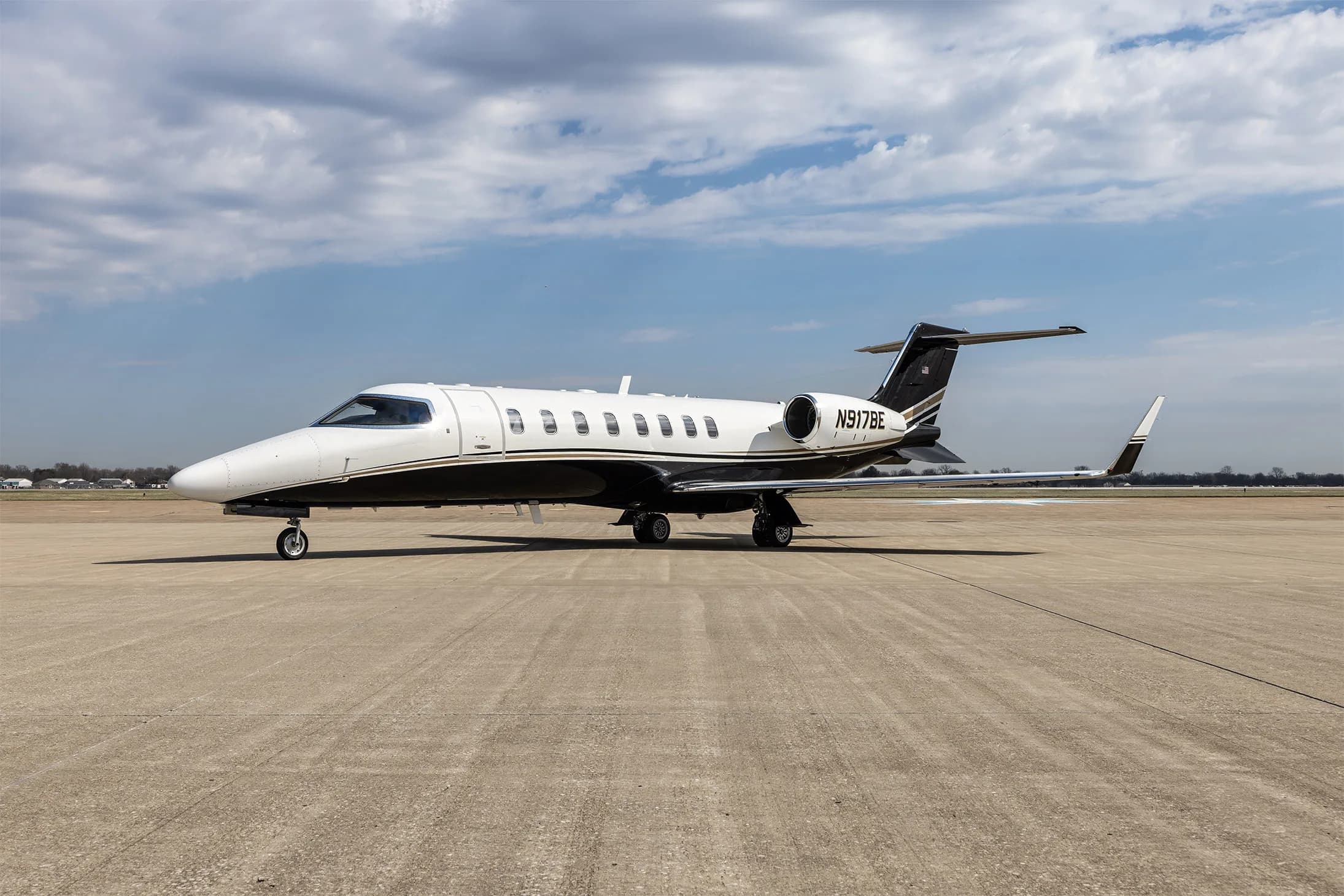 A Learjet 60 business jet with a white and black paint scheme parked on an airfield under a cloudy sky.