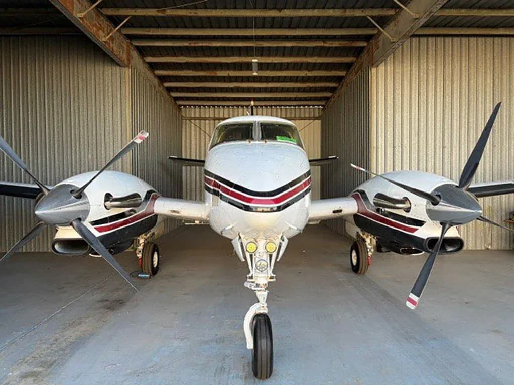 A white and red Beechcraft King Air C90 aircraft with registration N717JG parked in a hangar, viewed head-on.