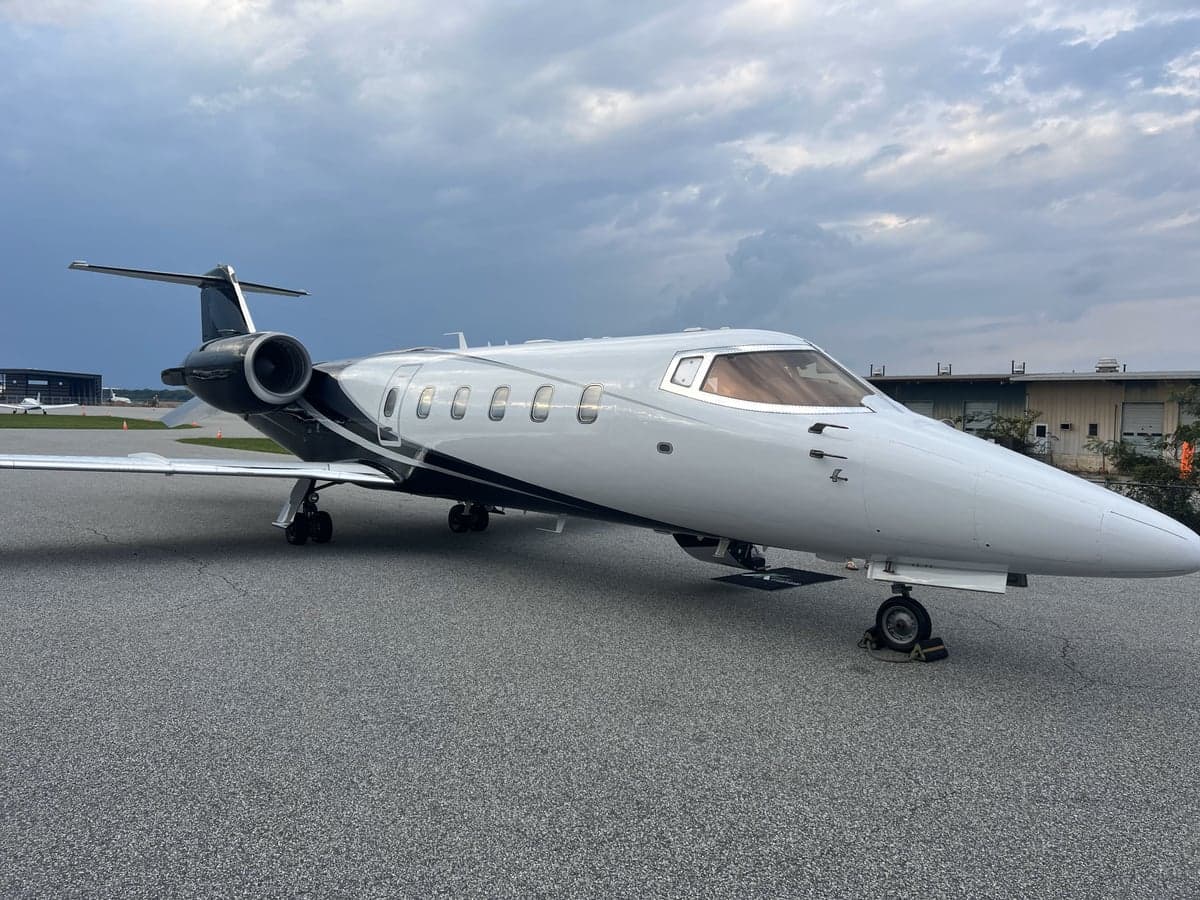 A Learjet aircraft is parked on the tarmac with a cloudy sky in the background.