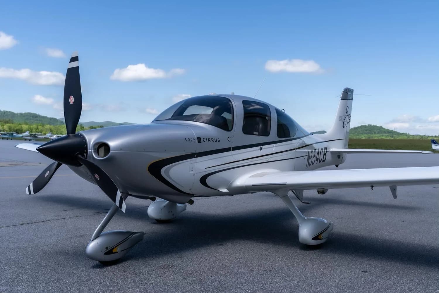 A close-up front three-quarter view of a silver and white Cirrus SR22T aircraft with registration N554CB on an airport tarmac.