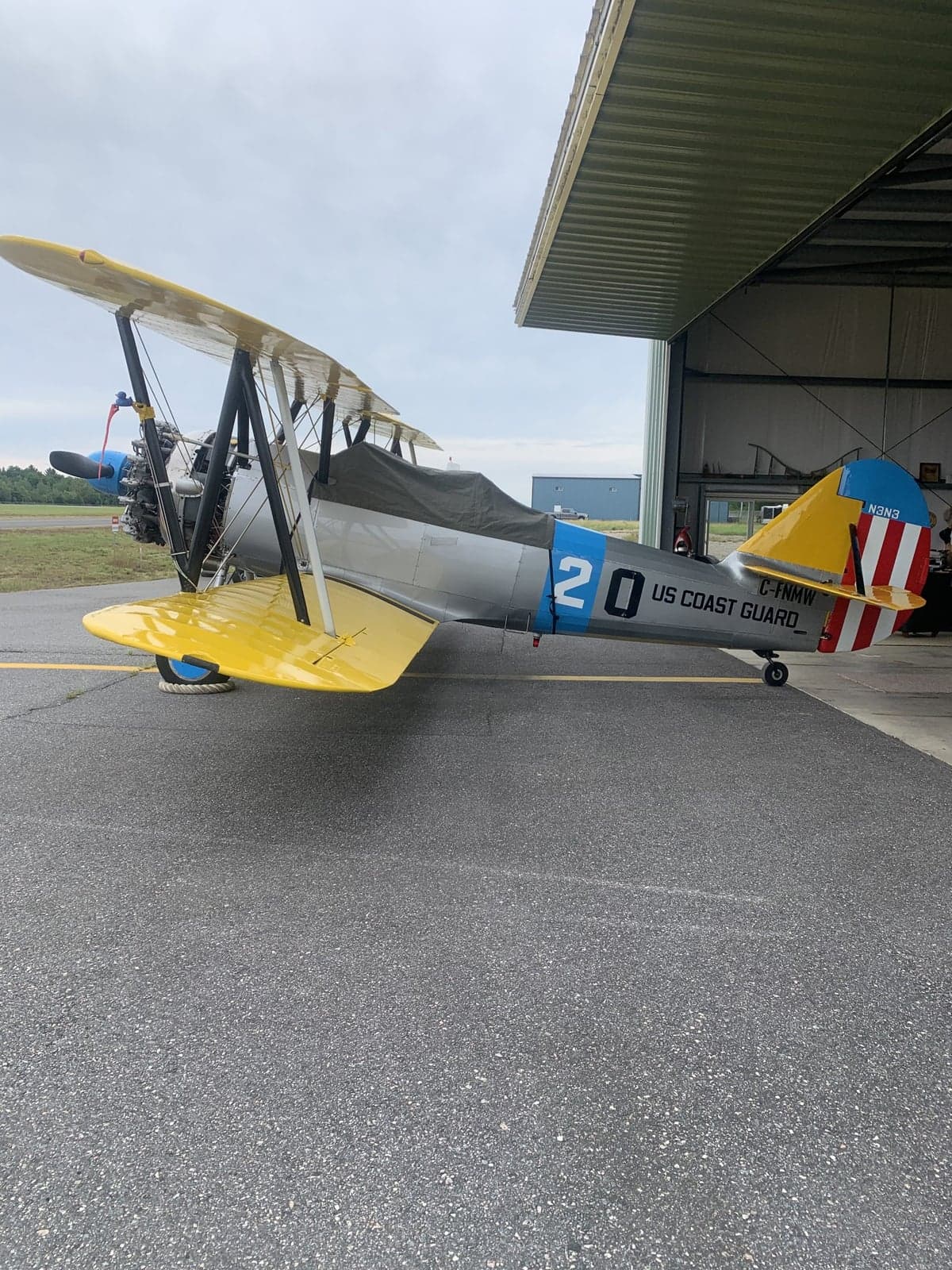 A yellow and silver biplane with US Coast Guard markings is parked near a hangar.