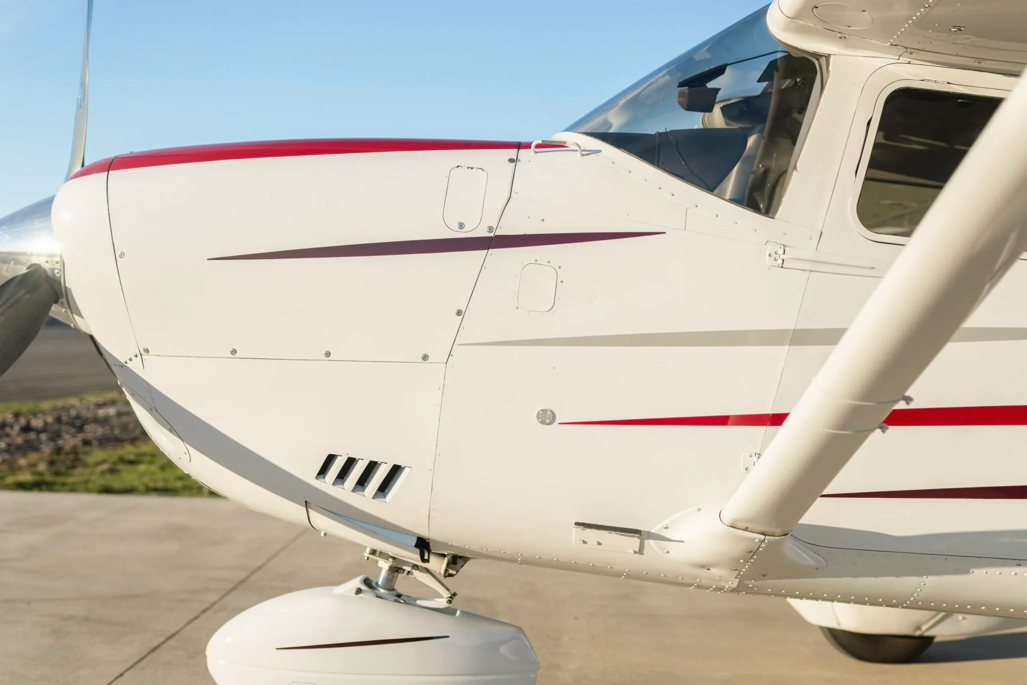 A close-up of the white nose and front fuselage of a Cessna aircraft, featuring red accents and engine vents.
