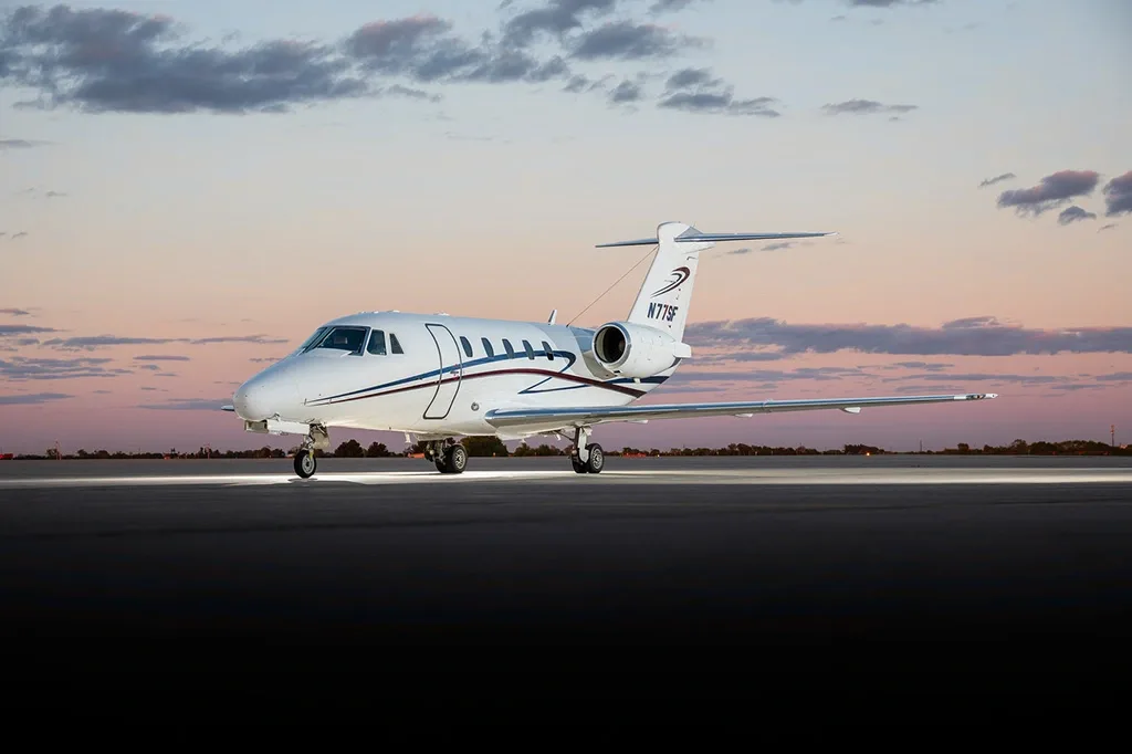 A white Cessna Citation business jet with blue and red stripes on the tail, parked on a tarmac at sunset.