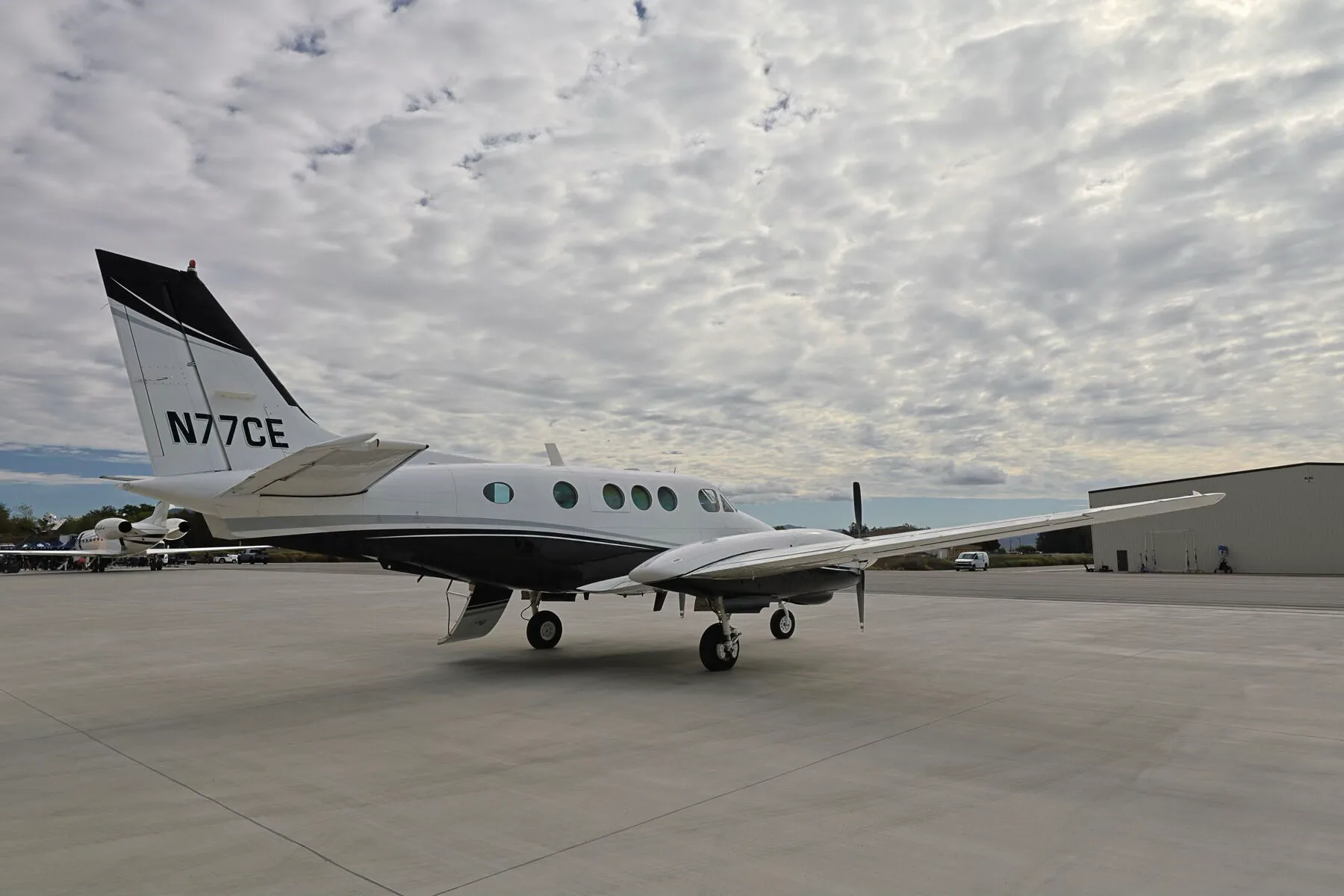 A left side view of the N77CE twin-engine turboprop aircraft on a wide airfield.