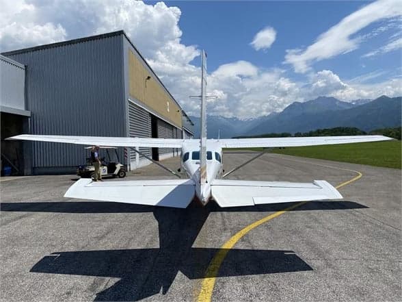 Rear view of a Cessna 210 Centurion aircraft on the tarmac in front of a hangar.
