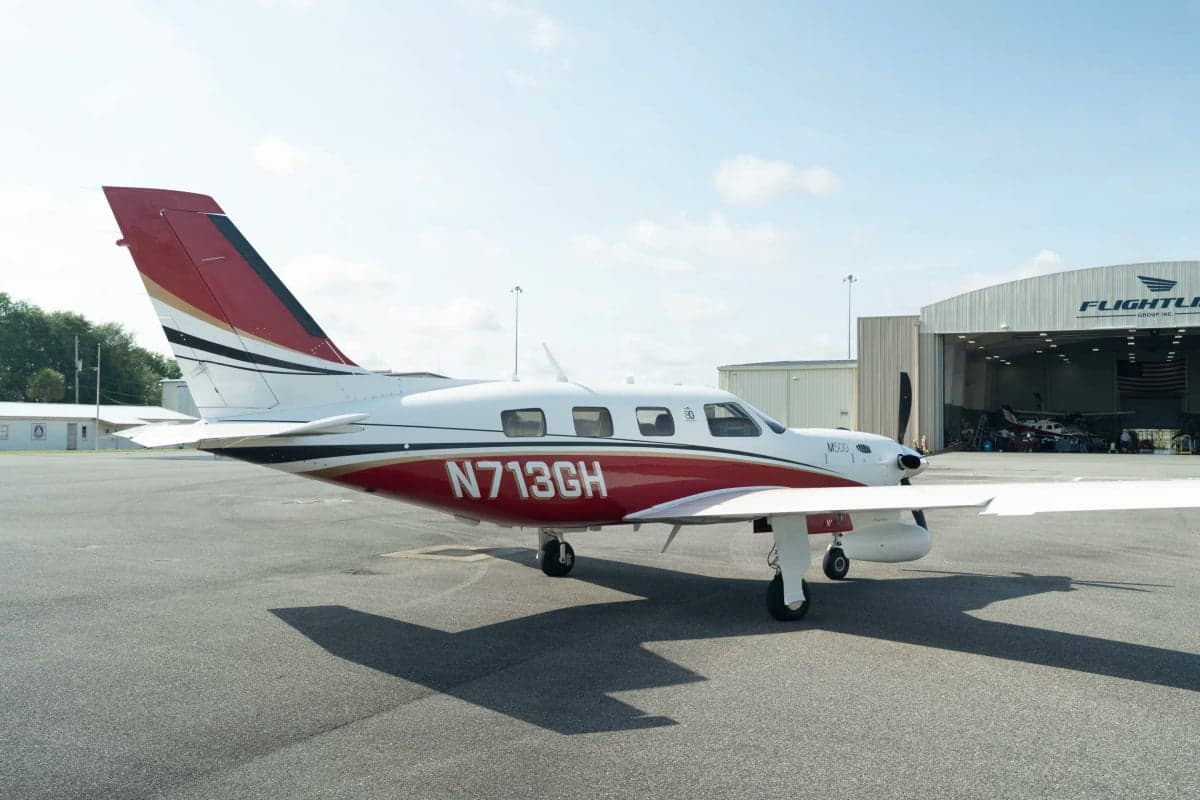 A white and red Piper M500 aircraft with registration N713GH parked on an asphalt tarmac, viewed from the front-right, with a hangar in the background.
