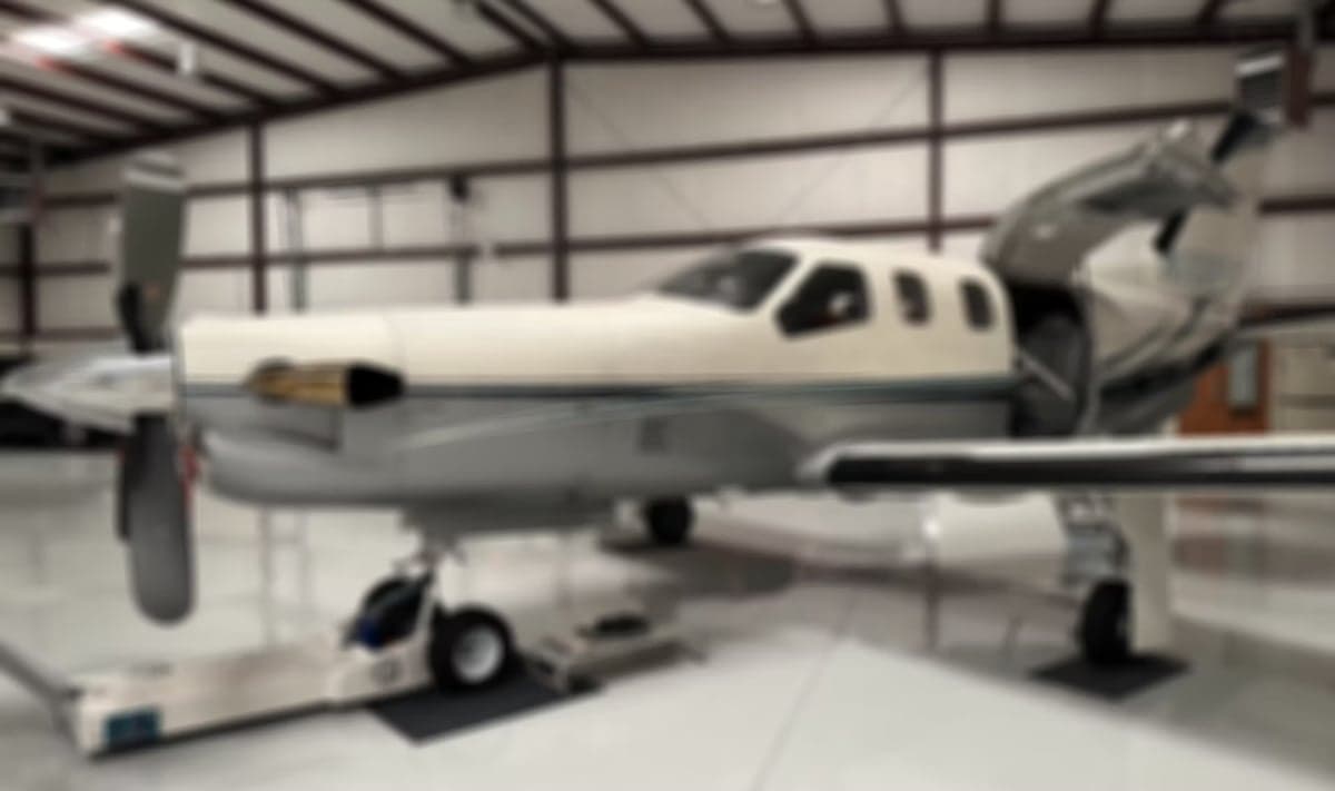 A blurred image of a TBM 930 aircraft parked inside a hangar.