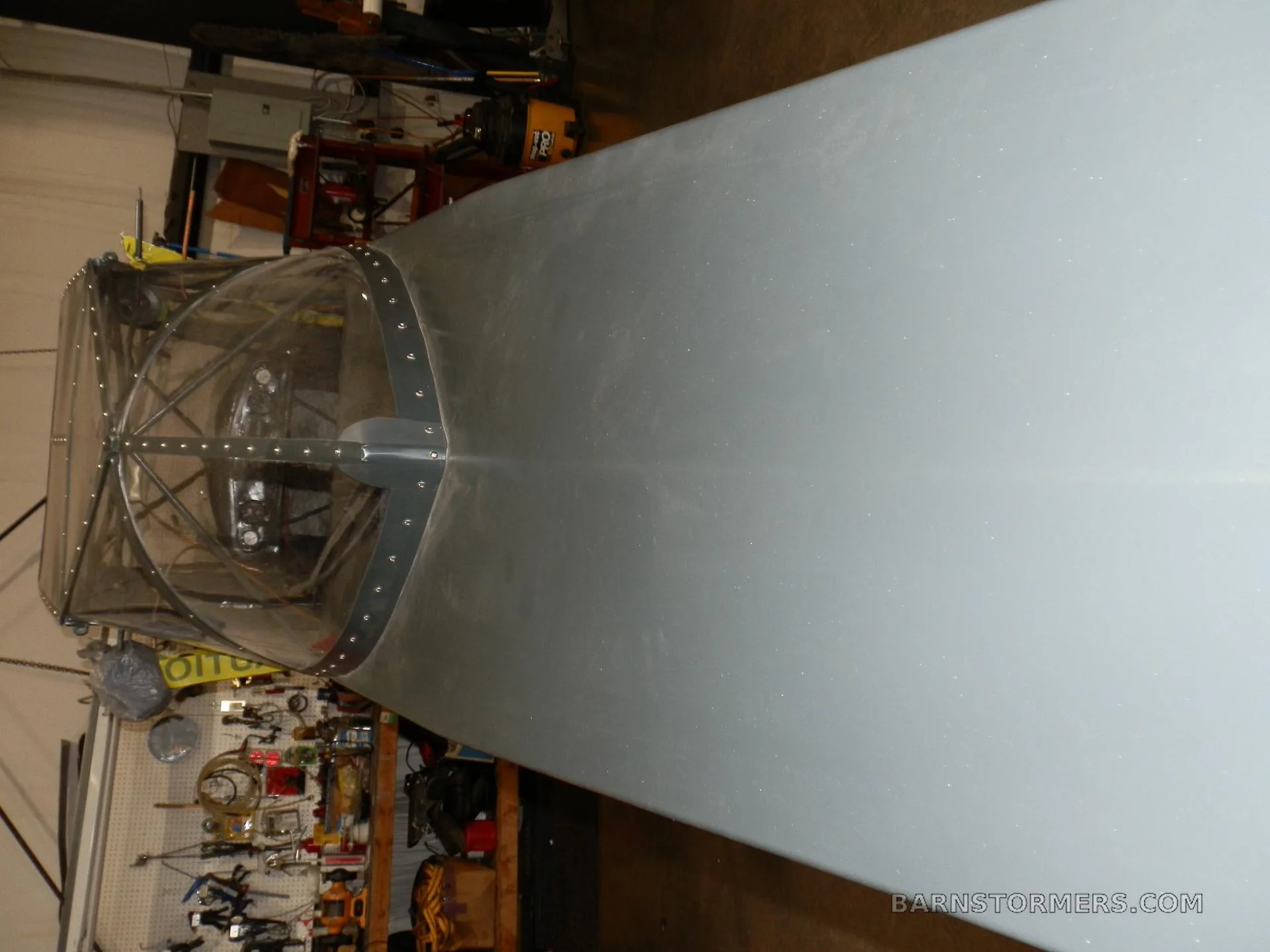 An overhead view looking down the light grey fuselage of an aircraft towards its clear bubble canopy.