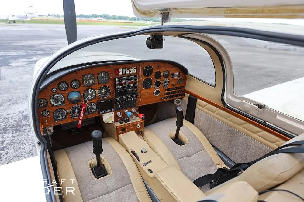 The cockpit of the aircraft with a wooden instrument panel, dual joysticks, and tan and beige seats.