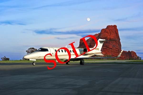 A Learjet 45XR aircraft with registration N345RL parked on the tarmac with a red rock formation in the background, marked with a 'SOLD' overlay.