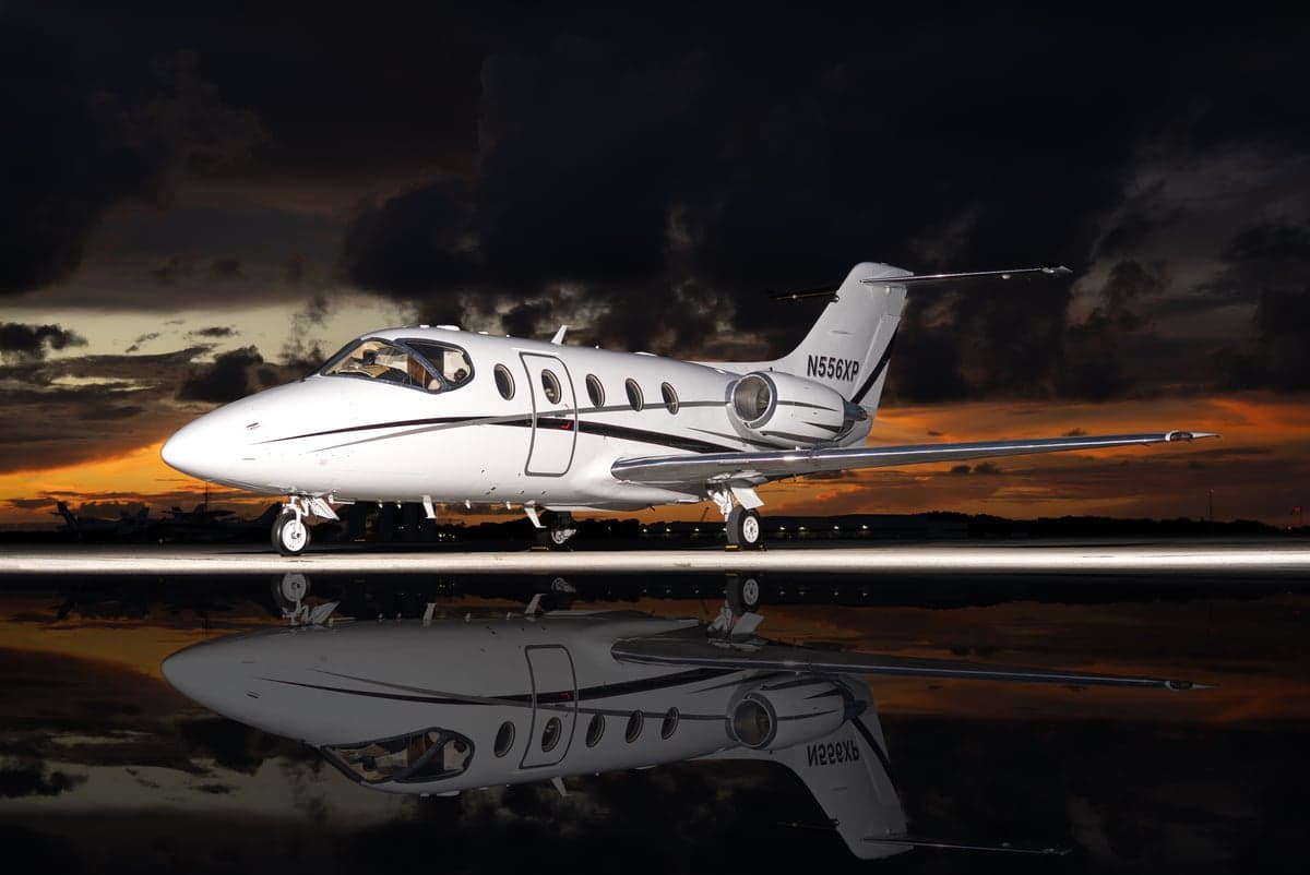 A white Learjet is reflected on the tarmac at sunset.