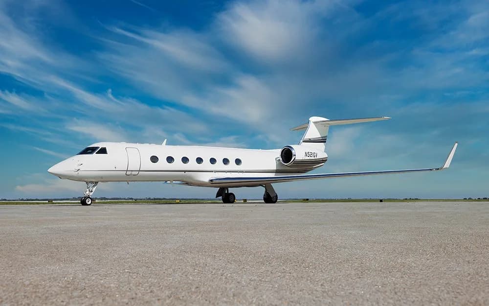 A white Gulfstream G550 business jet with a black stripe on the tail, parked on a tarmac under a blue sky.