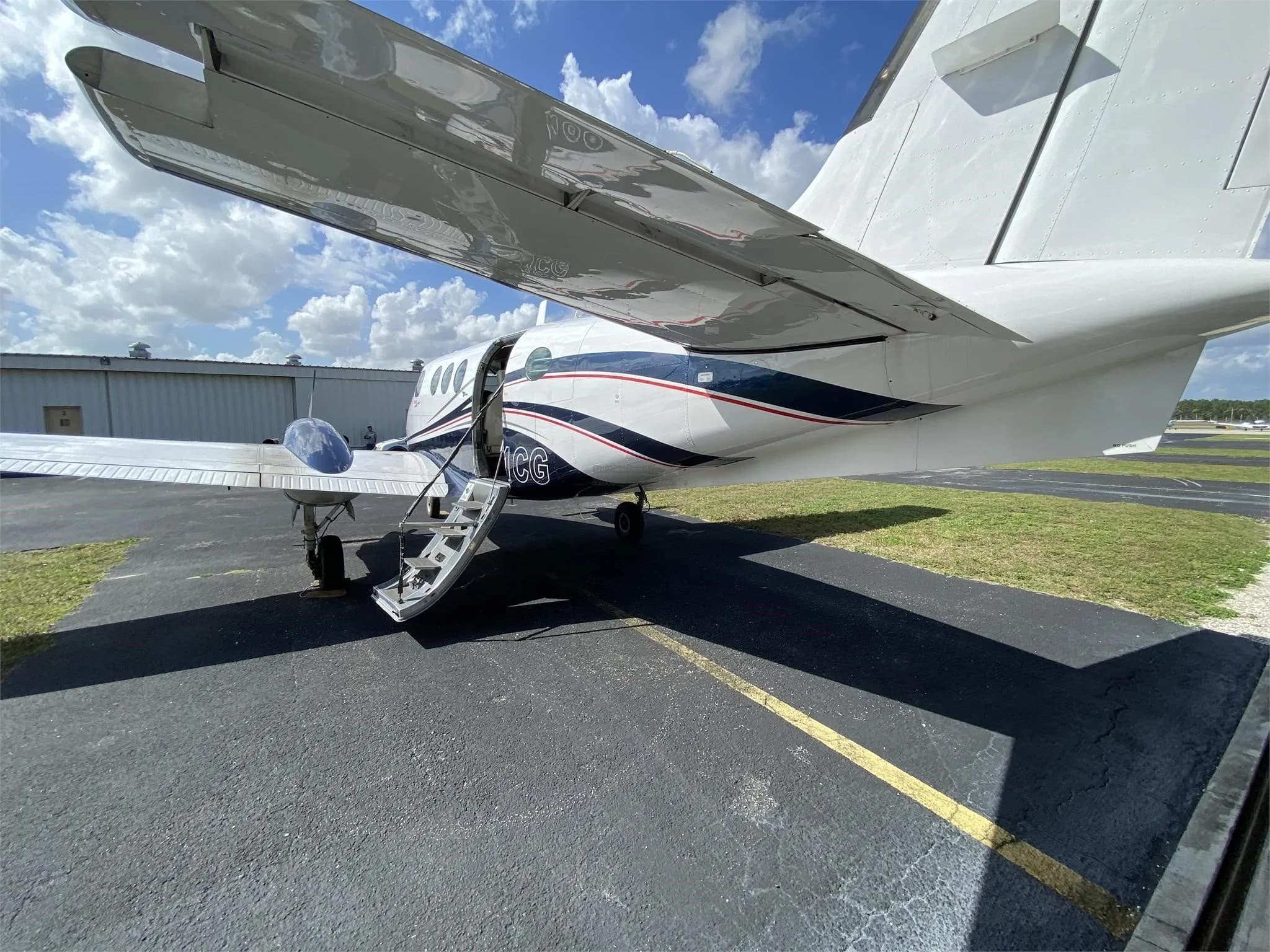 A close-up view of the rear fuselage and wing of the Beechcraft King Air N211CG, showing the open passenger door and stairs.