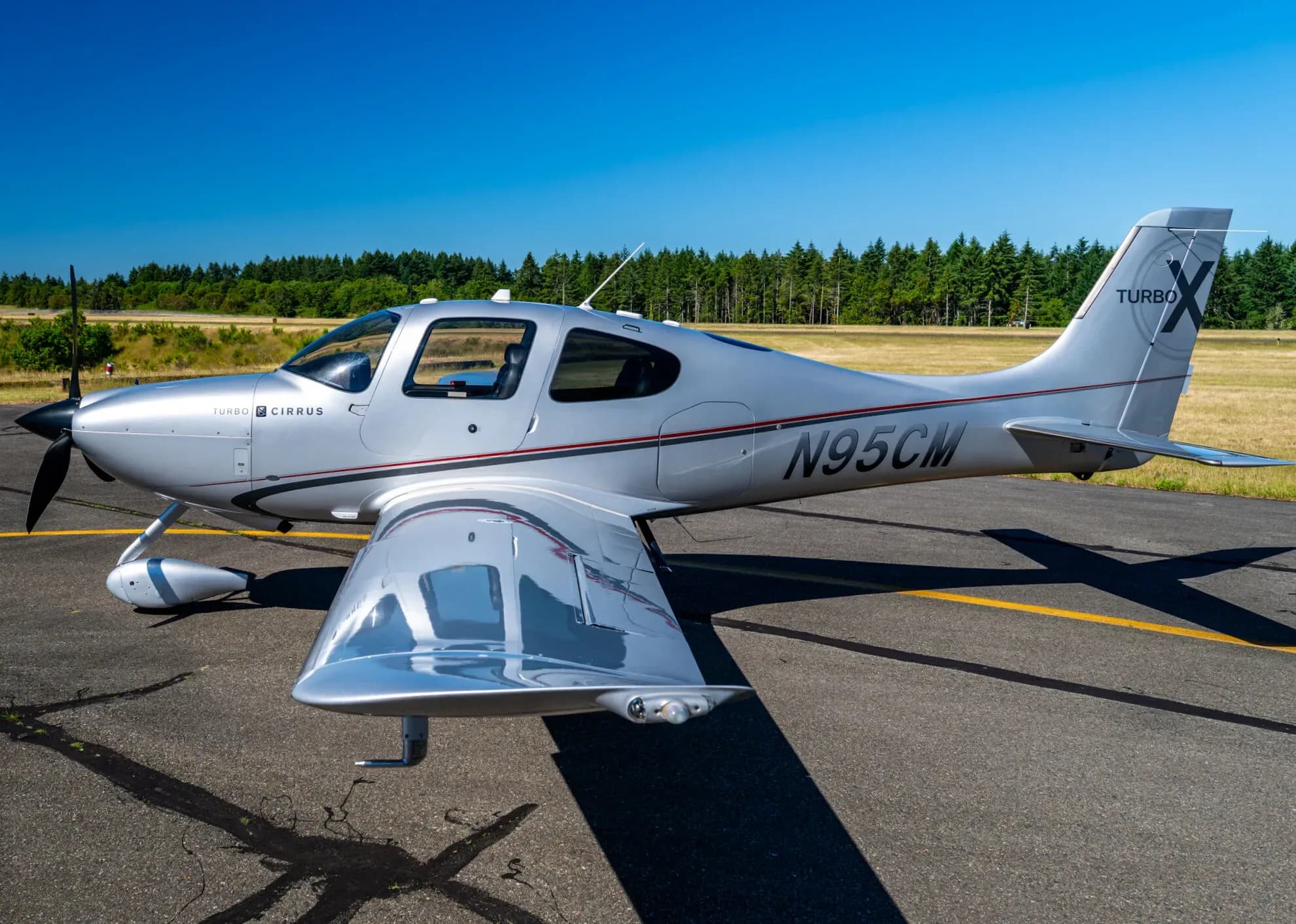 A silver Cirrus SR22T aircraft with registration N95CM parked on an airfield, viewed from the rear-side.