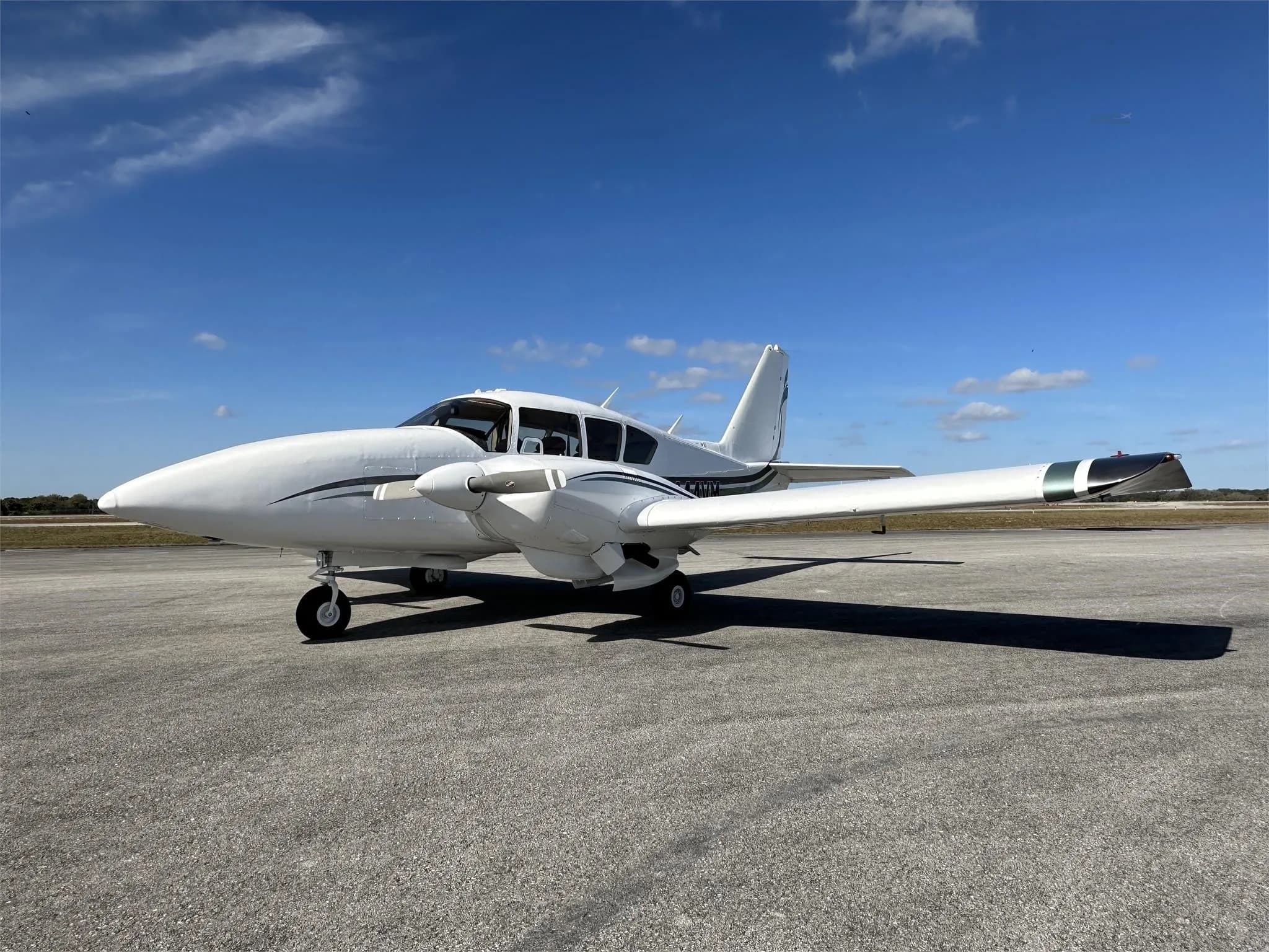 A front-side view of a white Piper aircraft with green and black stripes, registration N444VM, parked on an airfield.