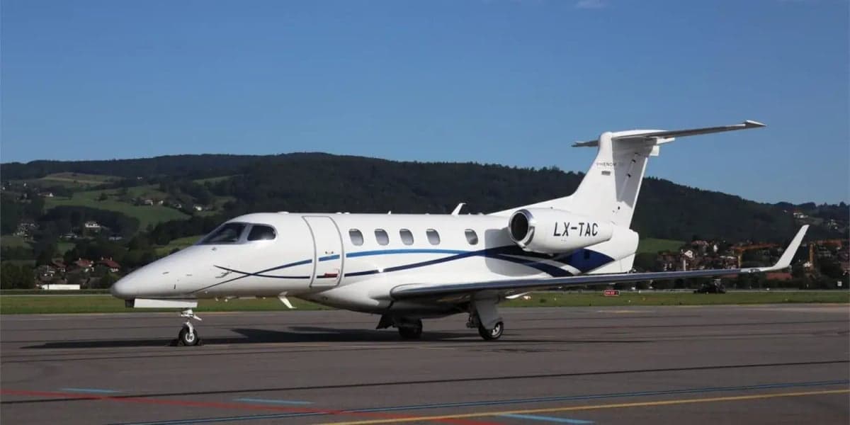 Side view of a white Phenom 300 aircraft with blue accents on the tarmac.