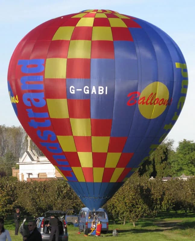 A red, blue, and yellow checkered hot air balloon with registration G-GABI being prepared on a grassy field.