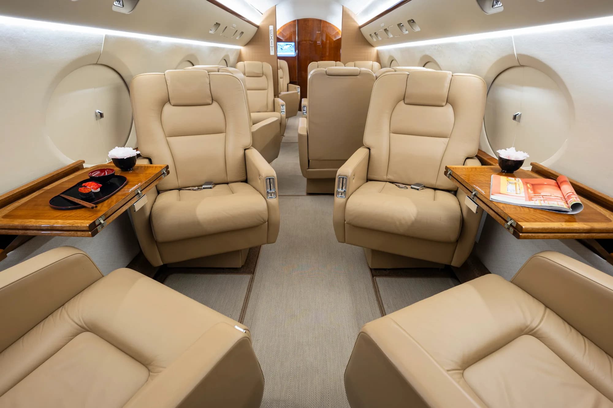 The interior of a private jet cabin with beige leather seats arranged in a club configuration.